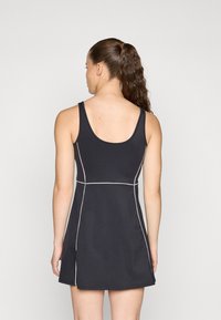 Vestido preto com alças de tanque, apresentando um corpete justo e uma saia em forma de evasé. Costura branca contrastante delineia o design. Textura suave.