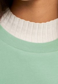 Sweat-shirt vert avec un col blanc texturé et côtelé. Tissu doux avec une finition lisse, doté d'un col rond et d'une coupe décontractée.