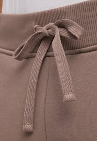 Braune Sweatpants mit einem gerippten Bund und einer geknoteten Kordel. Der Stoff hat eine glatte Textur und einen sanften Glanz.