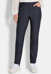 Marineblauwe broek met een gladde textuur, rechte snit, zijzakken en een subtiele glans. Gepaard met witte sneakers voor een casual look.