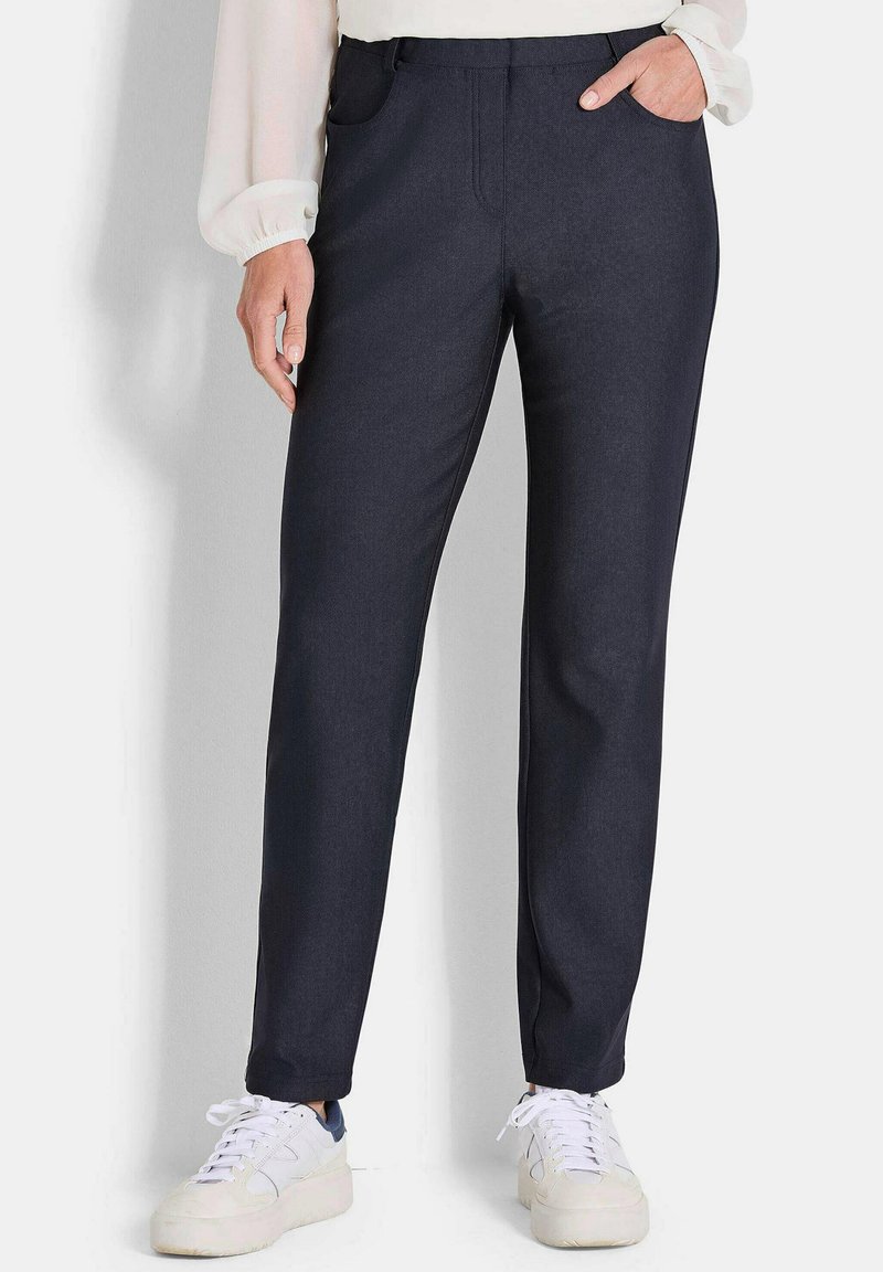 Marineblauwe broek met een gladde textuur, rechte snit, zijzakken en een subtiele glans. Gepaard met witte sneakers voor een casual look.
