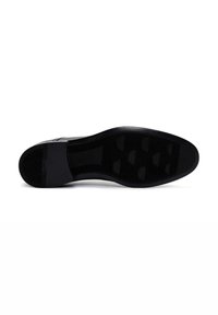 Semelle de chaussure en caoutchouc noir avec une surface texturée, présentant un motif en relief et des détails de préhension circulaires pour une meilleure traction.
