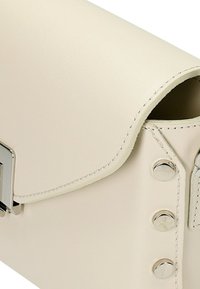 Beige leren clutch met een ronde klep, zilverkleurige hardware en decoratieve studs langs de rand. Gladde textuur met nette stikdetails.