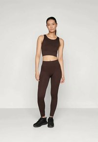 Bruin crop top en hooggetailleerde leggings gemaakt van rekbare stof, gecombineerd met zwarte sportschoenen. Eenvoudig, nauwsluitend ontwerp.