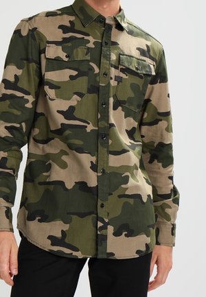 Chemise en camouflage à boutons dans des tons de vert et beige, dotée de deux poches poitrine, d'un col pointu et de manches longues avec poignets boutonnés.