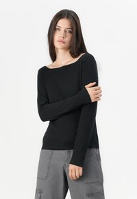 Top nero a maniche lunghe con scollatura ampia e vestibilità slim, realizzato in un tessuto morbido. Abbinato a pantaloni cargo grigi con ampie tasche laterali.