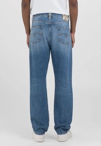 Jeans de mezclilla azul claro con un corte relajado, piernas rectas y dos bolsillos traseros. Presentan una etiqueta de marca visible en la cintura.