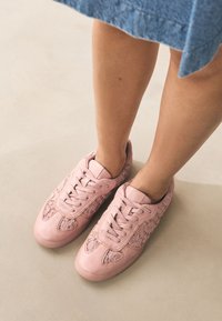 Baskets rose pâle en cuir et tissu, avec détails en dentelle, bout rond, semelle plate et design traditionnel à lacets.