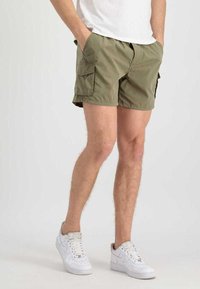 Khakifarbene Cargo-Shorts mit zwei Seitentaschen, elastischem Bund und lässigem Schnitt, kombiniert mit weißen Sneakers. Glattes, leichtes Material.