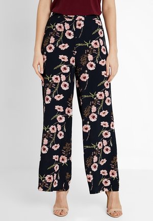 Marineblauwe wijde pantalons met roze bloemenprint, gedragen met een bordeauxrode top en beige open-toe hakken.