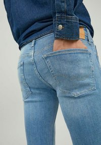 Vaqueros de denim azul claro con corte ajustado, que presentan bolsillos traseros con costuras curvadas y una etiqueta de cuero en la cintura.