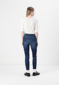 Blå denim skinny jeans med høy midje, baklommer og en tettsittende passform. Kombinert med en hvit t-skjorte med korte ermer og svarte sko.