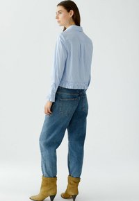Gestreiftes kurzes Oberteil in Blau und Weiß mit elastischem Bund, kombiniert mit lässigen blauen Jeans und bräunlichen, hochhackigen Stiefeletten.
