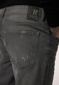 Jeans in denim grigio con una distintiva texture distressed, una toppa in pelle nera con "JP 1880" e un classico design a cinque tasche.