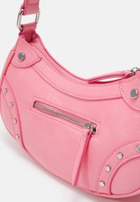 Rosa handväska i konstläder med rundad form, utrustad med ett blixtlåsförsett fack, silverfärgade nitar och en axelrem. Texturerad yta.