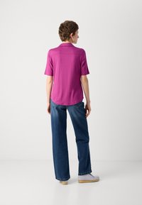 Fuksia polo skjorte med korte ermer, buet kant, kombinert med slitt blå denim jeans og lyse slip-on sko.