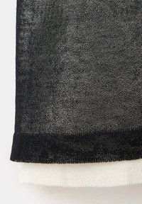 Gros plan d'un tissu tricoté noir et blanc en couches avec des fils fins visibles et des bords pliés.