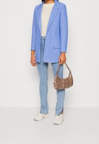 Light blue blazer with a textured design, beige top, light blue jeans with side slits, and a small brown snake print handbag. White sneakers.