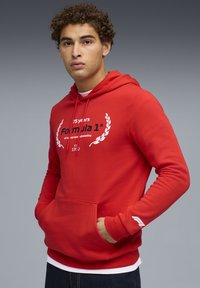 Rød hættebluse med en frontlomme, der har et hvidt Formel 1-logo og laurbær grafik. Ribbet manchetter og kant, lavet af jersey materiale.