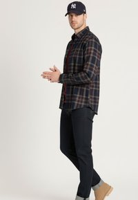 Camisa de franela a cuadros oscuros con tonos azul marino, rojo y verde, usada sobre una camiseta burdeos. Combinada con vaqueros oscuros y botas color canela.