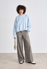 Lys blå oversized sweatshirt, grå vide bukser og stilige to-tonede sko. Bærer en lille beige håndtaske. Glatte materialer, afslappet pasform.
