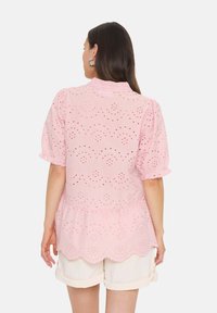 Top rosa a maniche corte con ritagli in pizzo floreale, scollo a balze e orlo scallop. Abbinato a pantaloni corti di colore chiaro.