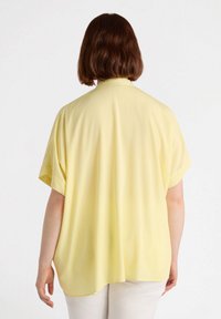 Blusa gialla a maniche corte realizzata in un tessuto morbido; vestibilità ampia con orlo arrotondato e silhouette rilassata. Design semplice, senza motivi o dettagli.