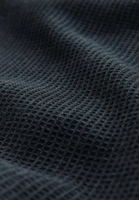 Tissu texturé foncé avec un motif en grille ; tissage étroitement serré créant une surface tactile ; apparence douce, légère et respirante.