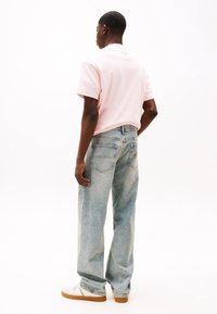 T-shirt en coton rose clair à manches courtes, associée à un jean bleu clair, ample, et des baskets blanches avec des semelles beige.