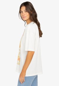 Camiseta blanca de gran tamaño con estampado gráfico floral colorido en el frente, mangas cortas y un corte relajado.