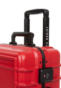 Red hard-shell suitcase with a textured surface, dual zippers, a black telescoping handle, and combination lock on the side.