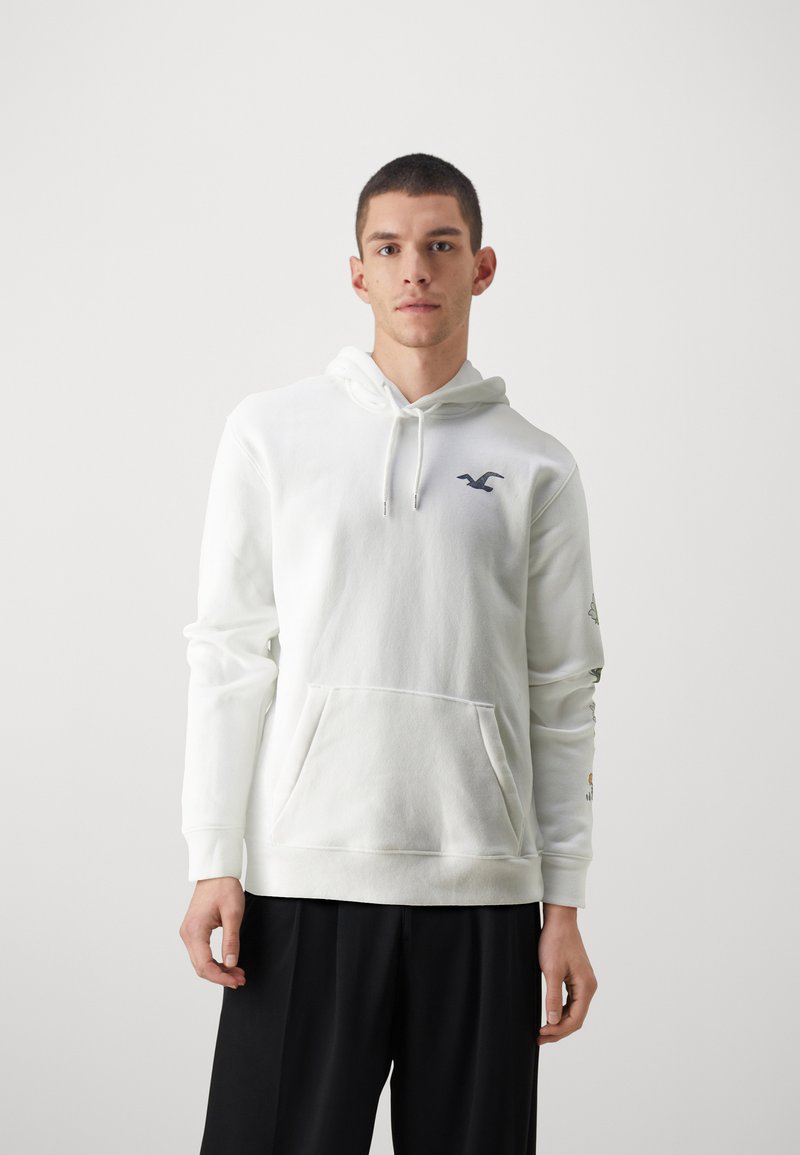 Weißer Kapuzenpullover mit Kordelzug, Fronttasche und navy Logo. Lange Ärmel verfügen auf einer Seite über bunte Grafiken. Weicher, strukturierter Stoff.