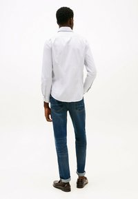 Camisa a rayas azul claro con mangas largas, puños abotonados y cuello extendido. Combinada con jeans azul oscuro y mocasines marrones.