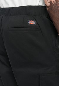 Close-up of black Dickies pants with elastic waistband and back welt pocket worn by person with freckled arm.