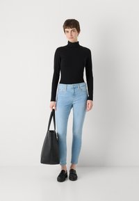 Un turtleneck noir à manches longues, un jean skinny bleu clair, des mocassins noirs et un sac fourre-tout noir. Tissus lisses et design ajusté.