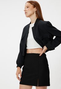 Mustat bomber-takit, joissa on ribbed-hihansuut, cropped-muotoilu ja kaksi etutaskua; yhdistetty mustaan, teksturoituun mini-hameseen, jossa on sivureikä.