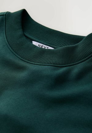 Pulover verde cu guler rotund, cu reazăm ribat și textură moale din bumbac. Eticheta de la guler scrie "NEXT". Culoare uniformă, netedă, fără modele.