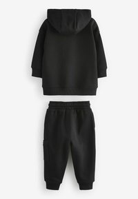 Ensemble en sweat à capuche noir et joggings en tissu doux. Le sweat à capuche a un cordon de serrage et des poignets côtelés ; les joggings possèdent une taille élastique et une poche latérale.