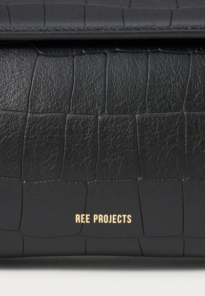 Bolso de cuero negro con un patrón de cocodrilo texturizado, que presenta un sutil logo dorado "REE PROJECTS" cerca de la parte inferior. Acabado suave y diseño elegante.