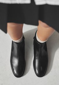 Zwarte enkellaarsjes van leer met een gladde afwerking, elastische zijpanelen, afgeronde neuzen en een lage hak, gecombineerd met licht gestructureerde sokken.