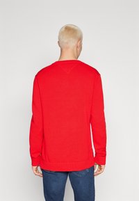 Roter gestrickter Pullover mit geripptem Saum und Bündchen, runder Ausschnitt und Seitennähten. Sanfte Textur, schlichtes Design und einfarbig.