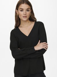 Blusa preta de manga longa com decote em V, em tecido texturizado, com detalhes em botões nos punhos, combinada com uma silhueta suave e ajustada.