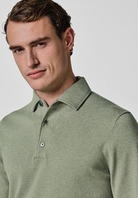 Hellgrünes Polohemd mit klassischem Kragen, Drei-Knopf-Leiste und strukturiertem Stoff. Verfügt über eine figurbetonte Silhouette und dezente Bündchen.