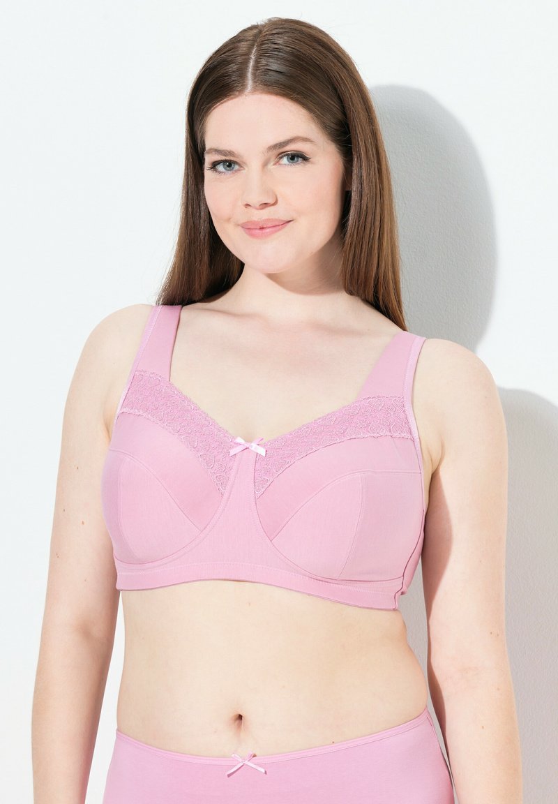 Vaaleanpunainen rintaliivi, jossa on leveät hihnat, pitsikoristelu ylhäällä ja pieni satiininen nauha keskellä. Pehmeä kangas ja tukevat ominaisuudet.