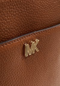 Sac en cuir texturé marron avec un logo "MK" doré et un accent cousu le long du bord supérieur.