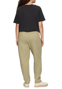 Zwarte cropped t-shirt met een ruwe zoom, gecombineerd met licht olijfgroene joggers. Losse pasvorm met een elastische tailleband, gedragen met beige instap schoenen.