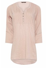 Tunic lunga a maniche lunghe rosa chiaro con scollatura arrotondata, chiusura a bottoni e dettagli di pieghe verticali; tessuto morbido con una finitura leggermente strutturata.