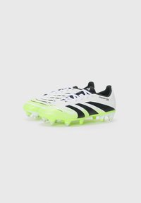 Des crampons de football blancs et noirs avec des accents verts, présentant une tige texturée, un laçage et de multiples crampons pour une meilleure traction.