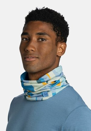 Joven con camisa azul y un tubular para el cuello estampado y colorido sobre un fondo liso.
