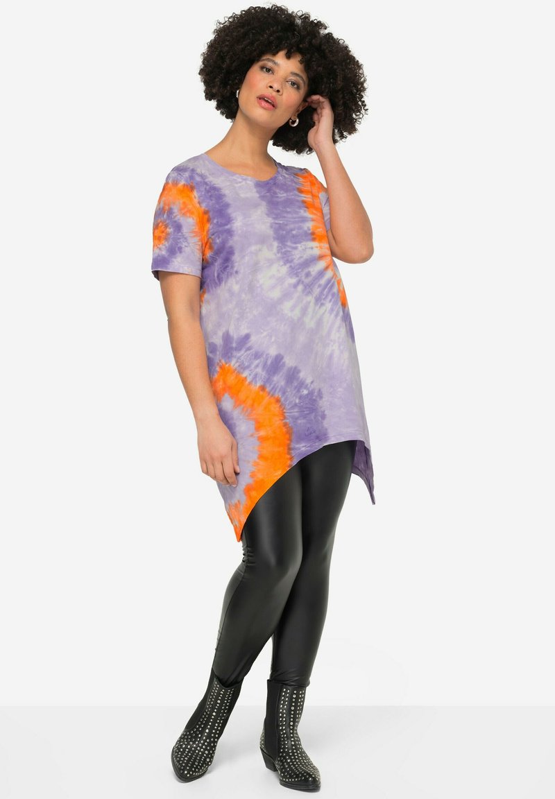 Paarse en oranje tie-dye t-shirt met korte mouwen en een asymmetrische zoom, gecombineerd met zwarte leggings en genagelde enkelboots.